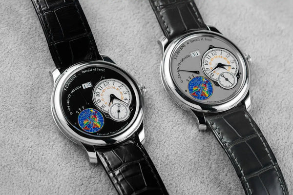 Two luxury watches with intricate designs on a gray surface